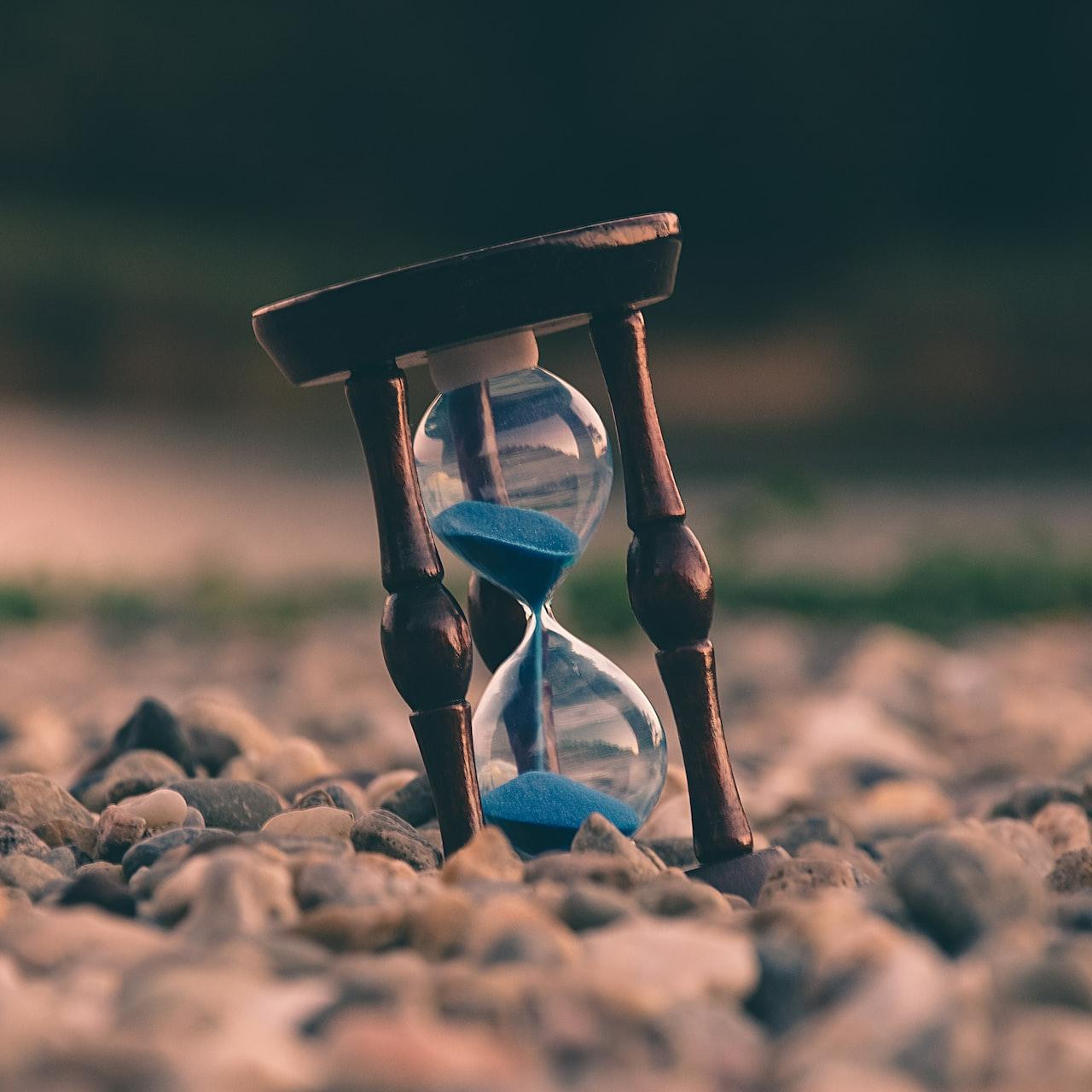 selective focus photo of brown and blue hourglass on stones